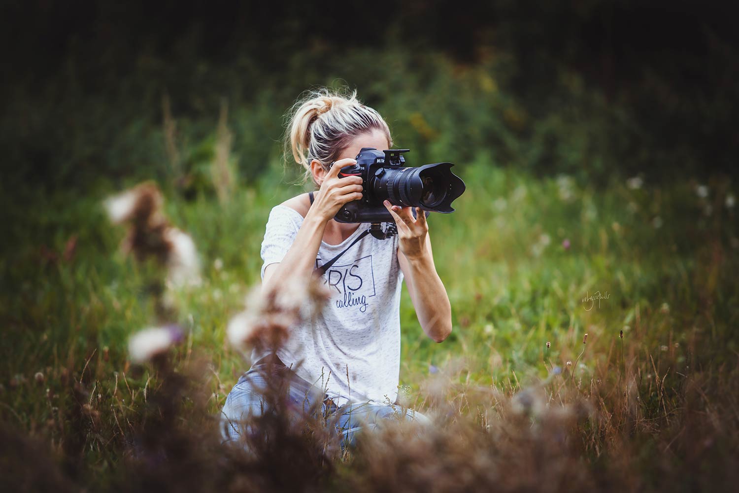 Pferdefotografin sitz im Gras und fokussiert mit ihrer Kamera das Model an