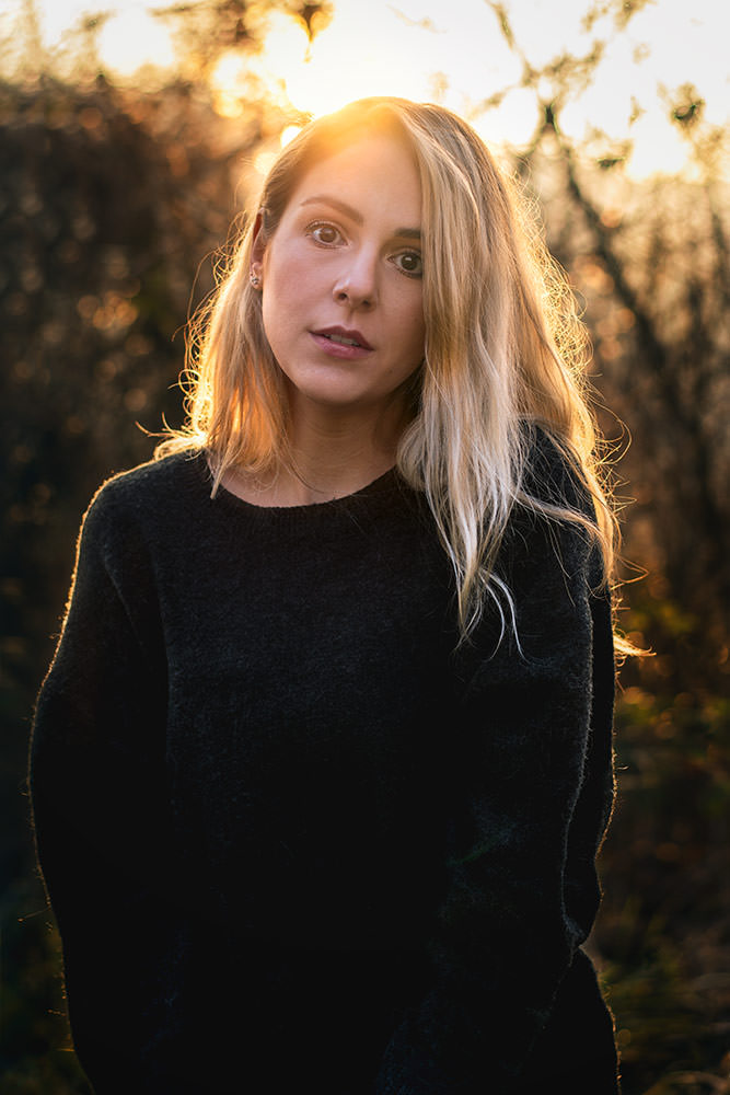 Porträt einer jungen Frau mit blonden Haaren im Sonnenunterganglicht, die in die Kamera schaut.