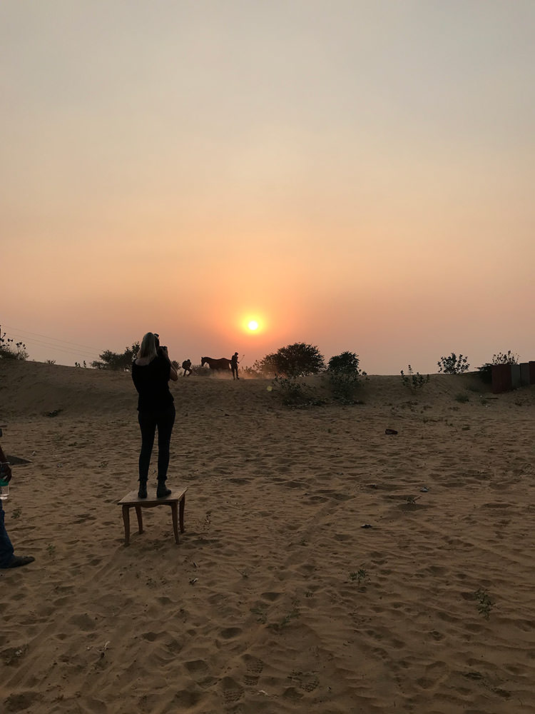 Eine Fotografin steht auf einem Hocker in der Wüste, um bei Sonnenuntergang ein Pferd zu fotografieren.