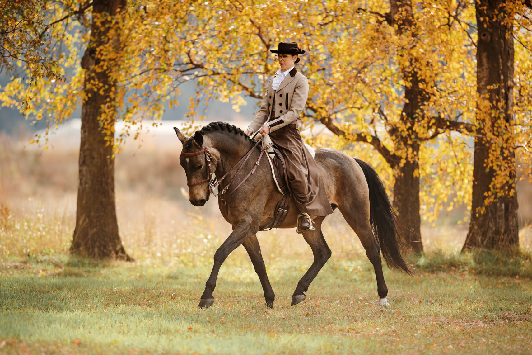 Eine Reiterin in traditioneller Reitkleidung reitet durch einen herbstlichen Wald.